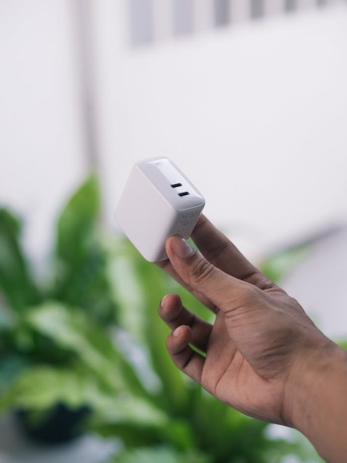 A hand holds a white USB adapter outdoors, with green foliage in the background.